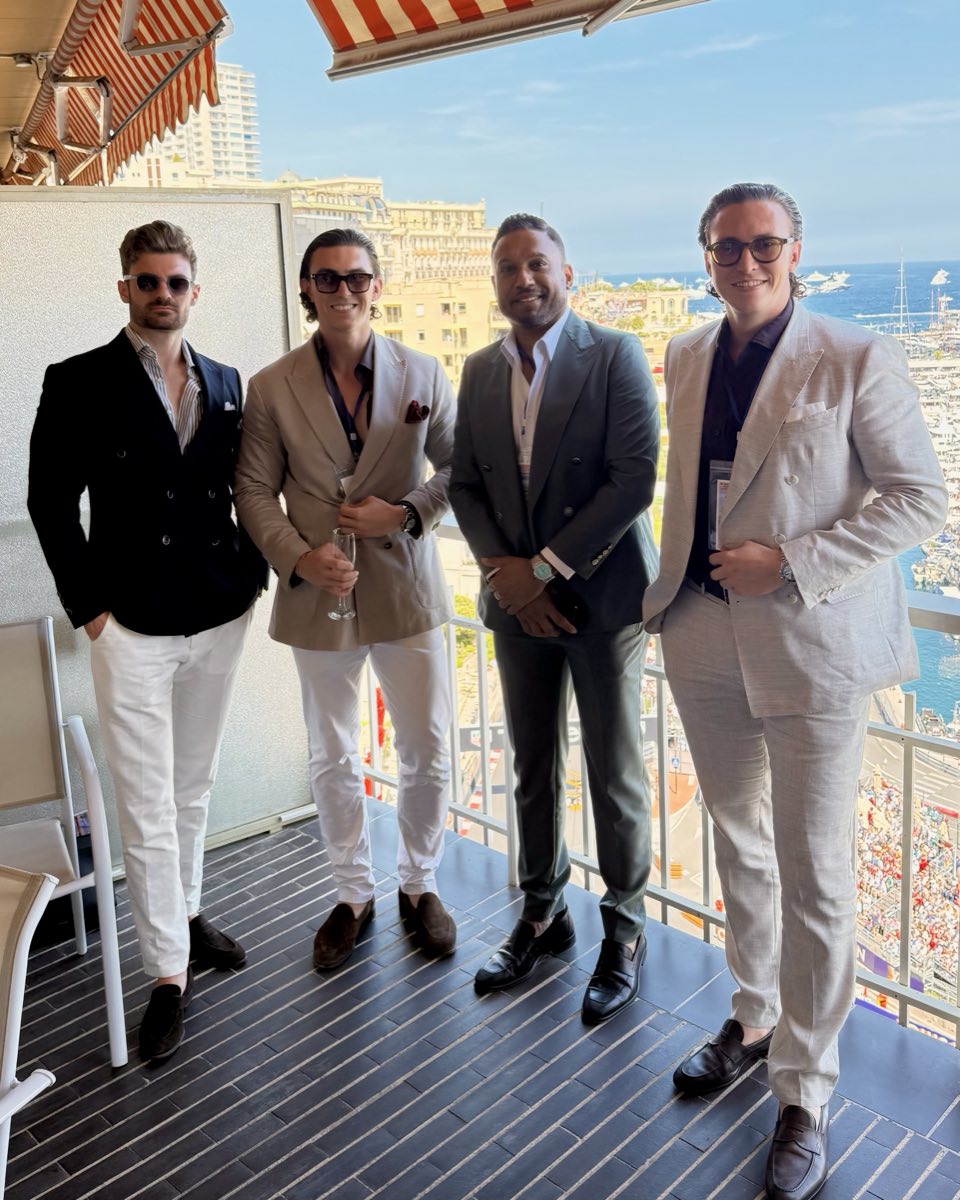 Jürgen and Matthias Nussbaumer with two guests on a balcony with a red and white striped awning above the harbour of Monaco during the Grand Prix